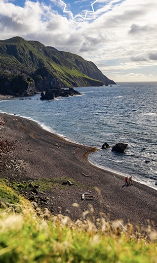 Two travellers slowly explore the beach in Green Gardens.