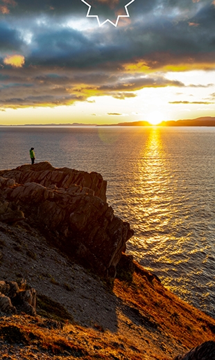 A person watches from the coast as the sun rises over Harbour Mille. 