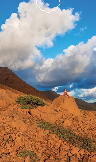 A traveller sits on a red rock in the Tablelands.