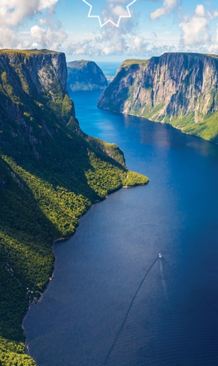 A boat navigates through the green cliffs and on the blue waters of Western Brook Pond Fjord.